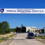 Entrance arch for Parcul Industrial Gorj S.A. over a road, car approaching on a sunny day with blue sky.