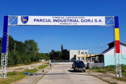 Entrance arch for Parcul Industrial Gorj S.A. over a road, car approaching on a sunny day with blue sky.