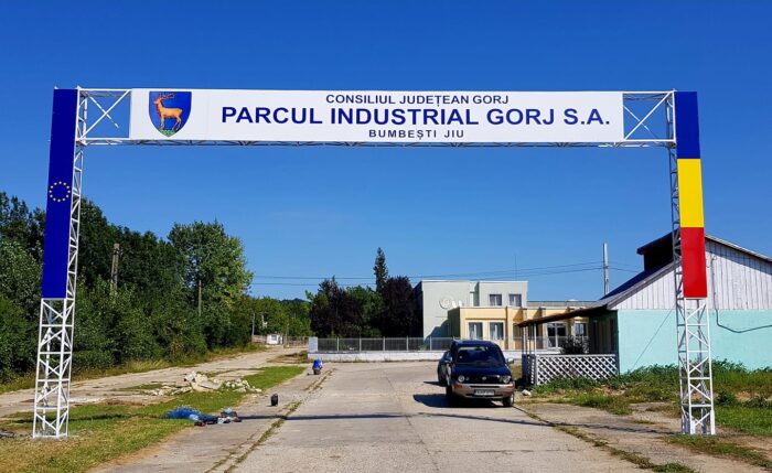 Entrance arch for Parcul Industrial Gorj S.A. over a road, car approaching on a sunny day with blue sky.