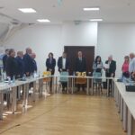 Group of professionals standing around a long conference table in a bright meeting room with water bottles on the table.