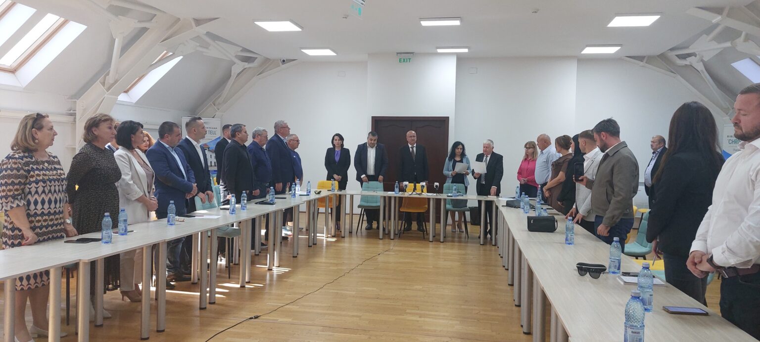 Group of professionals standing around a long conference table in a bright meeting room with water bottles on the table.