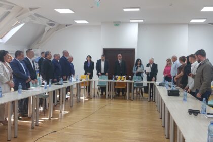 Group of professionals standing around a long conference table in a bright meeting room with water bottles on the table.
