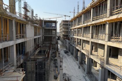 Large construction site with concrete structures, scaffolding, and tower cranes under a clear blue sky