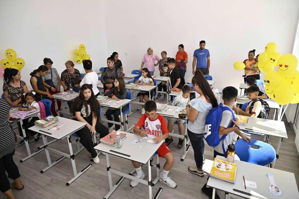 799784595_2284020075688381_4819124803752458899_n - Jurnalul Olteniei – Știri din Craiova și Oltenia Classroom full of kids at desks with adults guiding them; yellow smiley balloons decorate the room in corners.