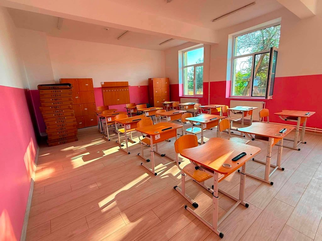 800098078_1646254080203059_5848823336894335905_n - Jurnalul Olteniei – Știri din Craiova și Oltenia Bright classroom with pink lower walls, wooden desks and chairs, and large open windows letting in sunlight.