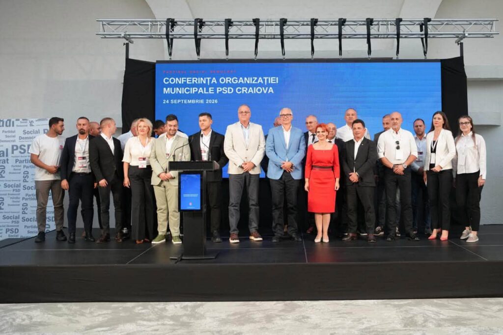 Group of people on a stage in front of a blue screen reading 'CONFERINȚA ORGANIZAȚIEI MUNICIPALE PSD CRAIOVA' at a 2026 conference.