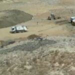 Construction site with dirt piles and several trucks, including white dump trucks, on a dusty excavated area.