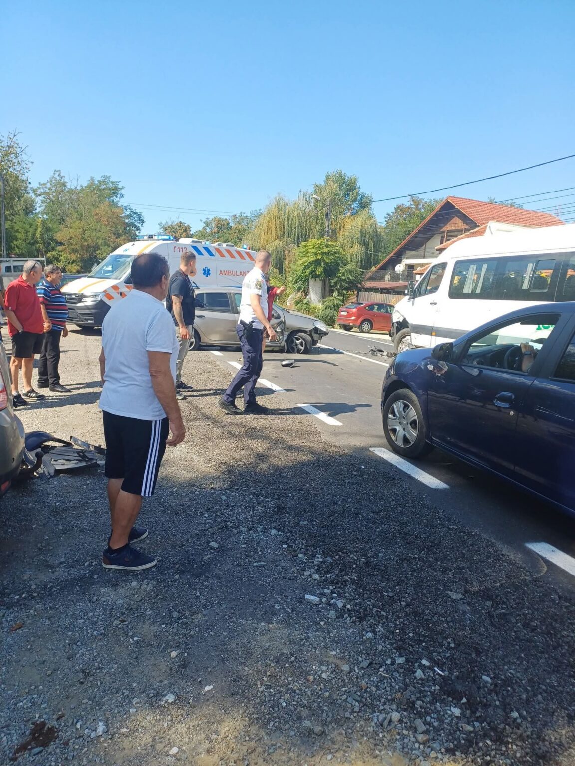 FB_IMG_1789559351855 - Jurnalul Olteniei – Știri din Craiova și Oltenia Group of bystanders and responders near a car crash on a sunny street; an ambulance and a damaged car are present.
