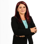 Professional woman with burgundy hair in a black blazer, arms crossed, wearing a light blue blouse, against a white background.