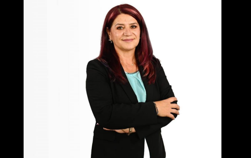 Professional woman with burgundy hair in a black blazer, arms crossed, wearing a light blue blouse, against a white background.