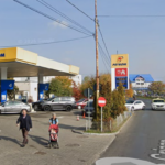 Petrom gas station with blue pump islands, several cars at the pumps, and pedestrians including a woman pushing a stroller on the sidewalk.