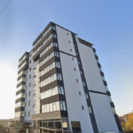 Modern white and dark-gray apartment building with multiple balconies on a sunny street.