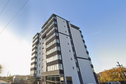 Modern white and dark-gray apartment building with multiple balconies on a sunny street.