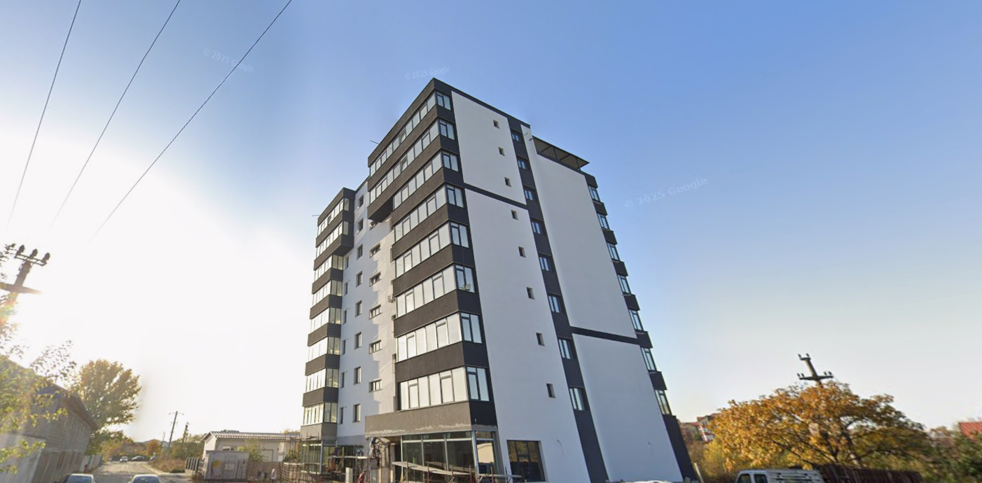 Modern white and dark-gray apartment building with multiple balconies on a sunny street.
