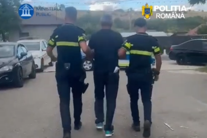 Three people walk down a street: two uniformed officers escorting a man in the middle, logos for Ministerul Public and Politia Romana visible.