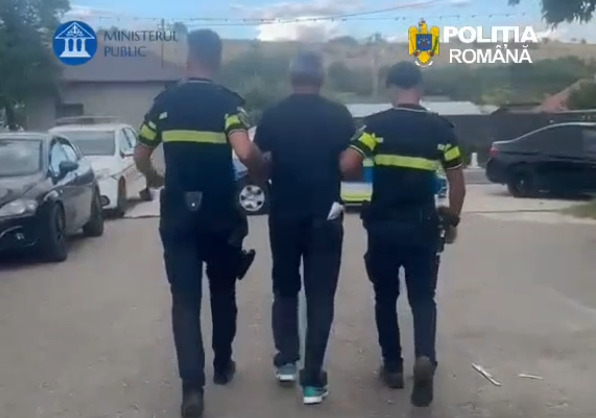 Screenshot 2026-09-15 133151 - Jurnalul Olteniei – Știri din Craiova și Oltenia Three people walk down a street: two uniformed officers escorting a man in the middle, logos for Ministerul Public and Politia Romana visible.