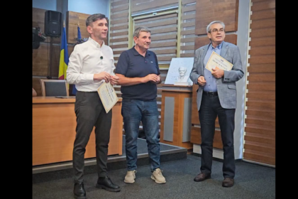 Three men in a formal room, two holding certificates during an award presentation; a Ukrainian flag and a framed photo are visible in the background.