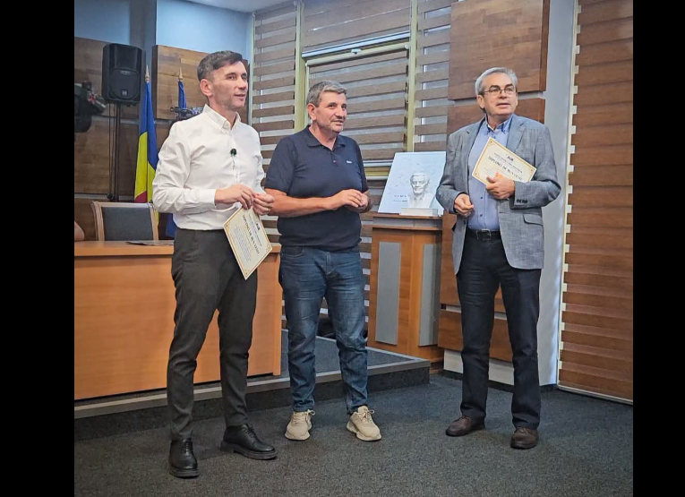 Three men in a formal room, two holding certificates during an award presentation; a Ukrainian flag and a framed photo are visible in the background.