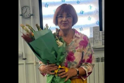 Woman in a floral blouse holding a large bouquet wrapped in green paper indoors.