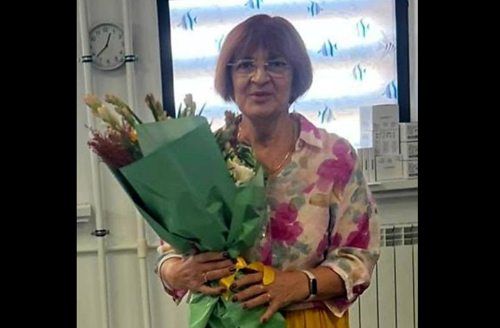 Woman in a floral blouse holding a large bouquet wrapped in green paper indoors.