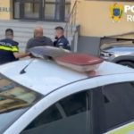 Two Romanian police officers accompany a man near a police car outside a government building with stairs in the background.