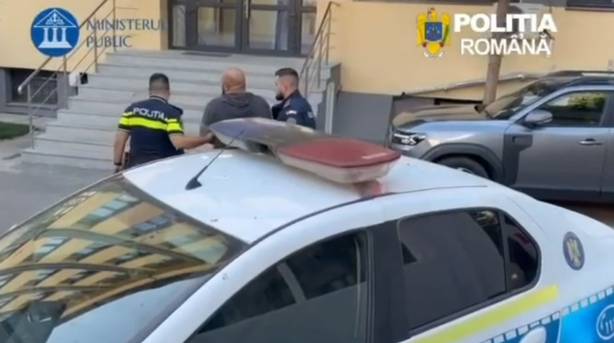 Two Romanian police officers accompany a man near a police car outside a government building with stairs in the background.