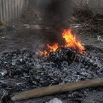 A pile of burning trash and debris in an outdoor alley, with orange flames, black smoke, and scorched rubble scattered on the ground.
