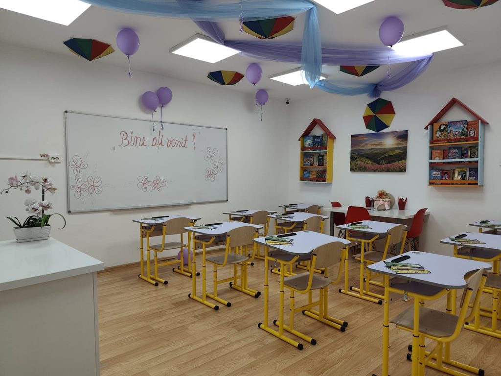 Classroom decorated for a welcome event with purple balloons, blue fabric garlands, and student desks grouped at tables.