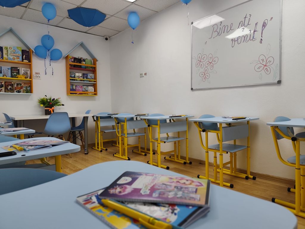 Blue balloon decorations in a classroom with magazines on desks and bookshelves along the wall, and a large whiteboard to the right.