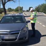 Police officer in a bright safety vest talks to the driver through the car window during a daytime traffic stop on a rural road