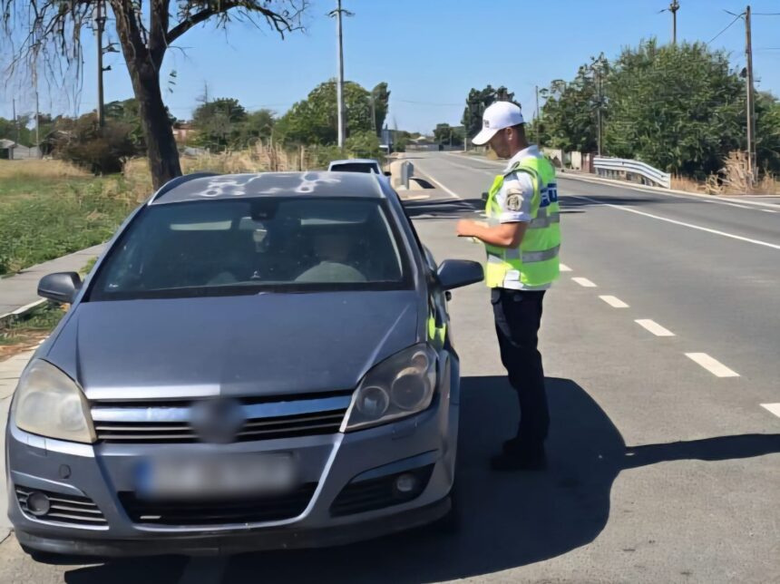 Police officer in a bright safety vest talks to the driver through the car window during a daytime traffic stop on a rural road