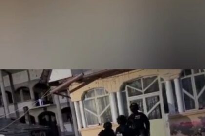 Romanian Police officers in tactical gear entering a building on a rainy day, under a police banner logo at top.
