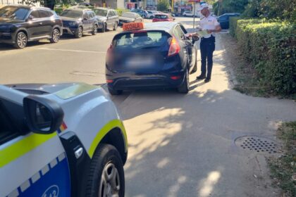 Police officer in a white uniform checks documents with a driver beside a blue car on a sunny street lined with parked cars.