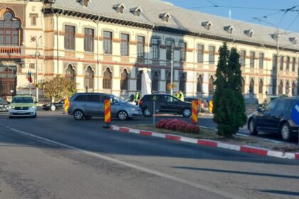 Historic city street with an ornate European-style building, multiple cars, and orange construction barriers under a clear blue sky.