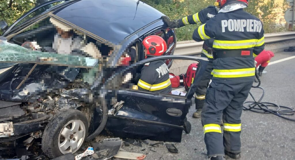 Firefighters in reflective gear aiding a driver inside a heavily damaged dark blue car after a highway crash.