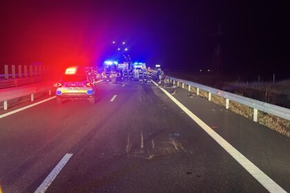 Nighttime highway crash scene with police car, ambulance, and firefighters tending to an incident in the distance with flashing lights.