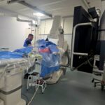 Operating room with a patient on a blue-draped table surrounded by large imaging equipment and cables for surgery. [Informative]
