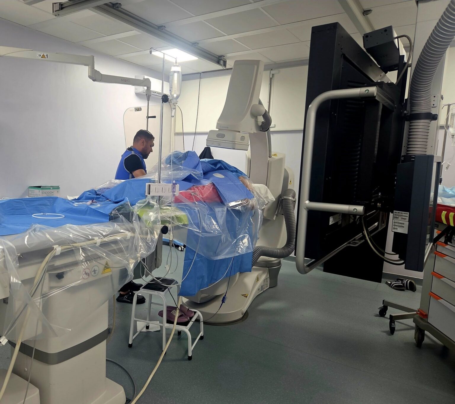 Operating room with a patient on a blue-draped table surrounded by large imaging equipment and cables for surgery. [Informative]