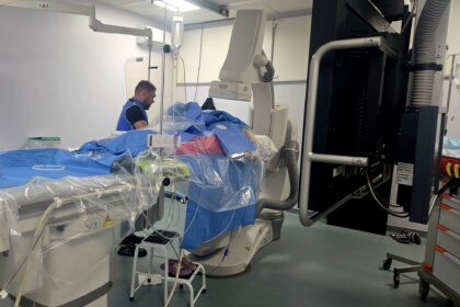 Operating room with a patient on a blue-draped table surrounded by large imaging equipment and cables for surgery. [Informative]