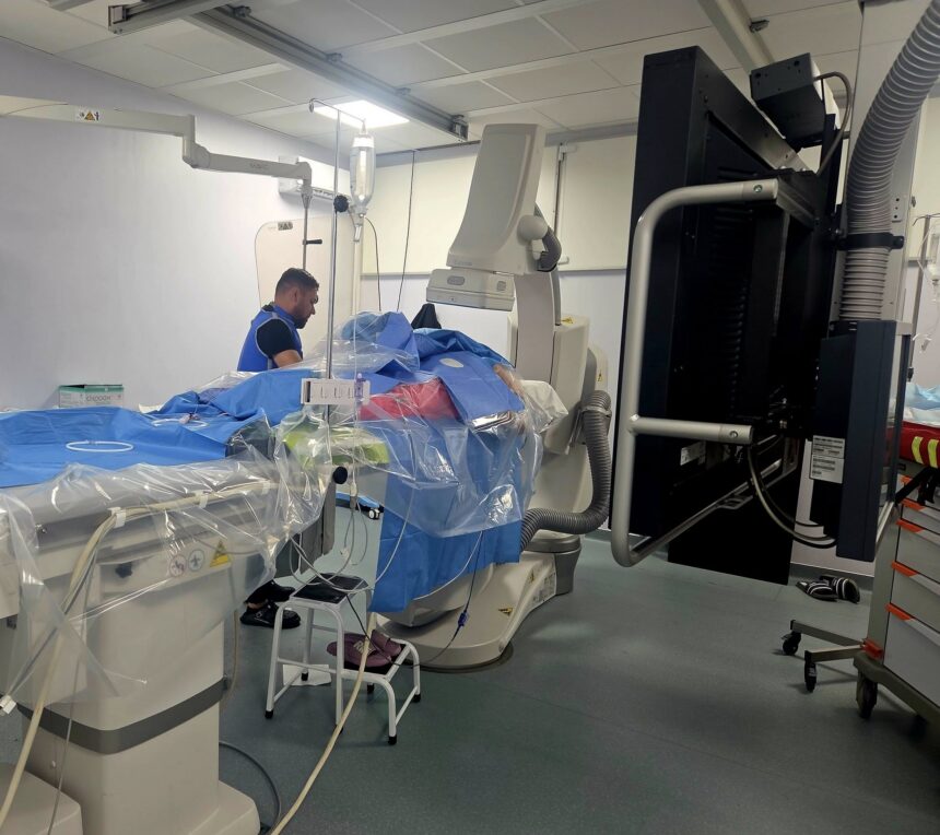 Operating room with a patient on a blue-draped table surrounded by large imaging equipment and cables for surgery. [Informative]