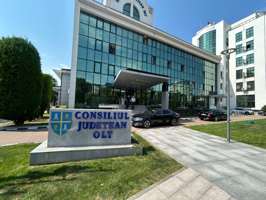 Modern government building with blue-tinted glass façade, entrance canopy, and a stone sign reading Consiliul Județean Olt in front.