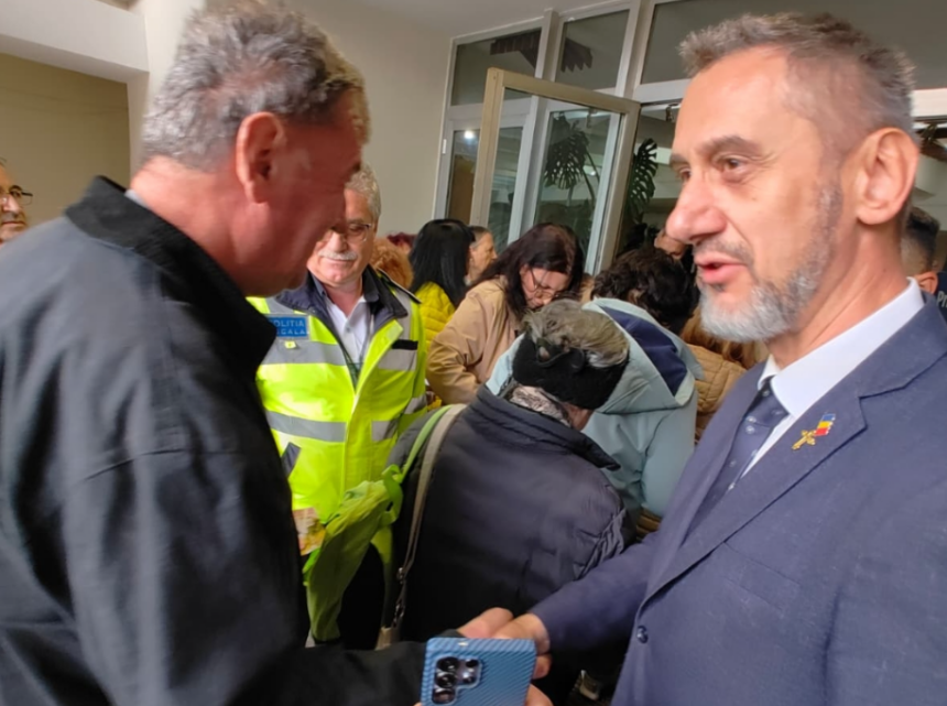 Two men shake hands in a crowded indoor event, with a police officer in a neon vest visible in the background.