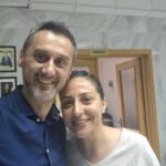 Two smiling adults posing for a selfie indoors, with a door labeled 'Prefect' in the background.