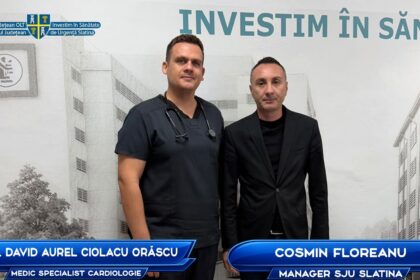 Two men pose for a photo in front of a medical-themed backdrop; one in scrubs with a stethoscope, the other in a black suit, with blue name banners at the bottom.