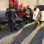Emergency responders and police carry an injured person on a stretcher outside a partially built concrete building.