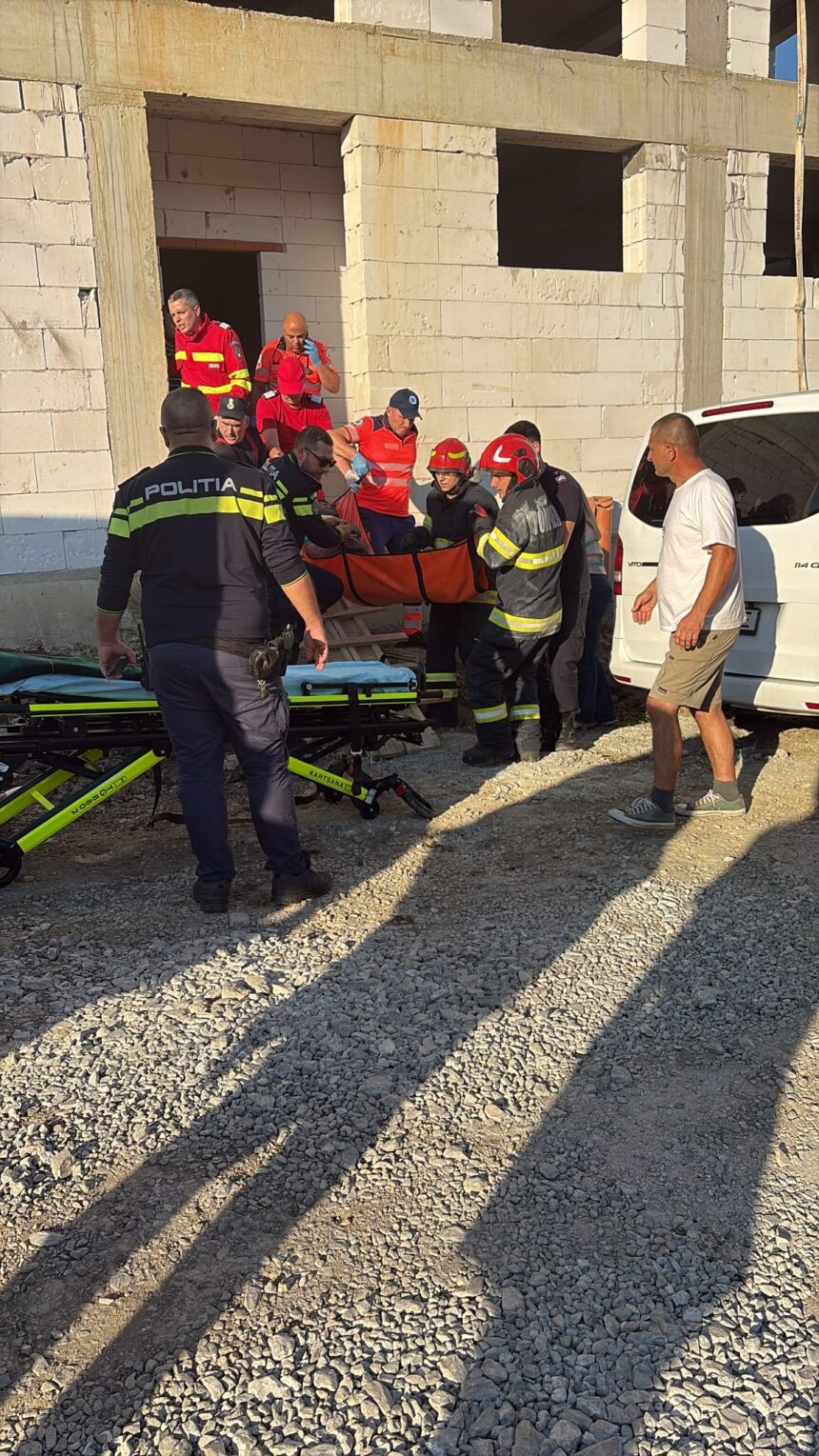 Emergency responders and police carry an injured person on a stretcher outside a partially built concrete building.