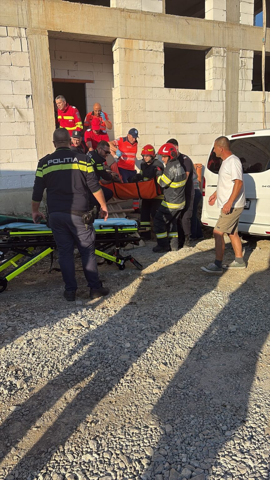 Emergency responders and police carry an injured person on a stretcher outside a partially built concrete building.