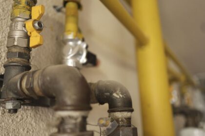 Close-up of a gas pipe with a yellow valve handle and threaded fittings mounted on a textured wall, with more piping in the background.