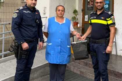 Two police officers hand a dark bag to a woman in a blue vest outside a building entrance.