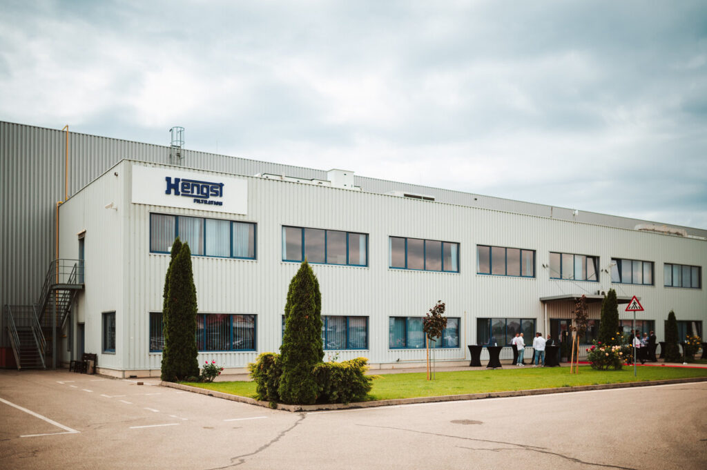 Industrial building with white corrugated facade, Hengst Filtration sign, and people near the entrance.